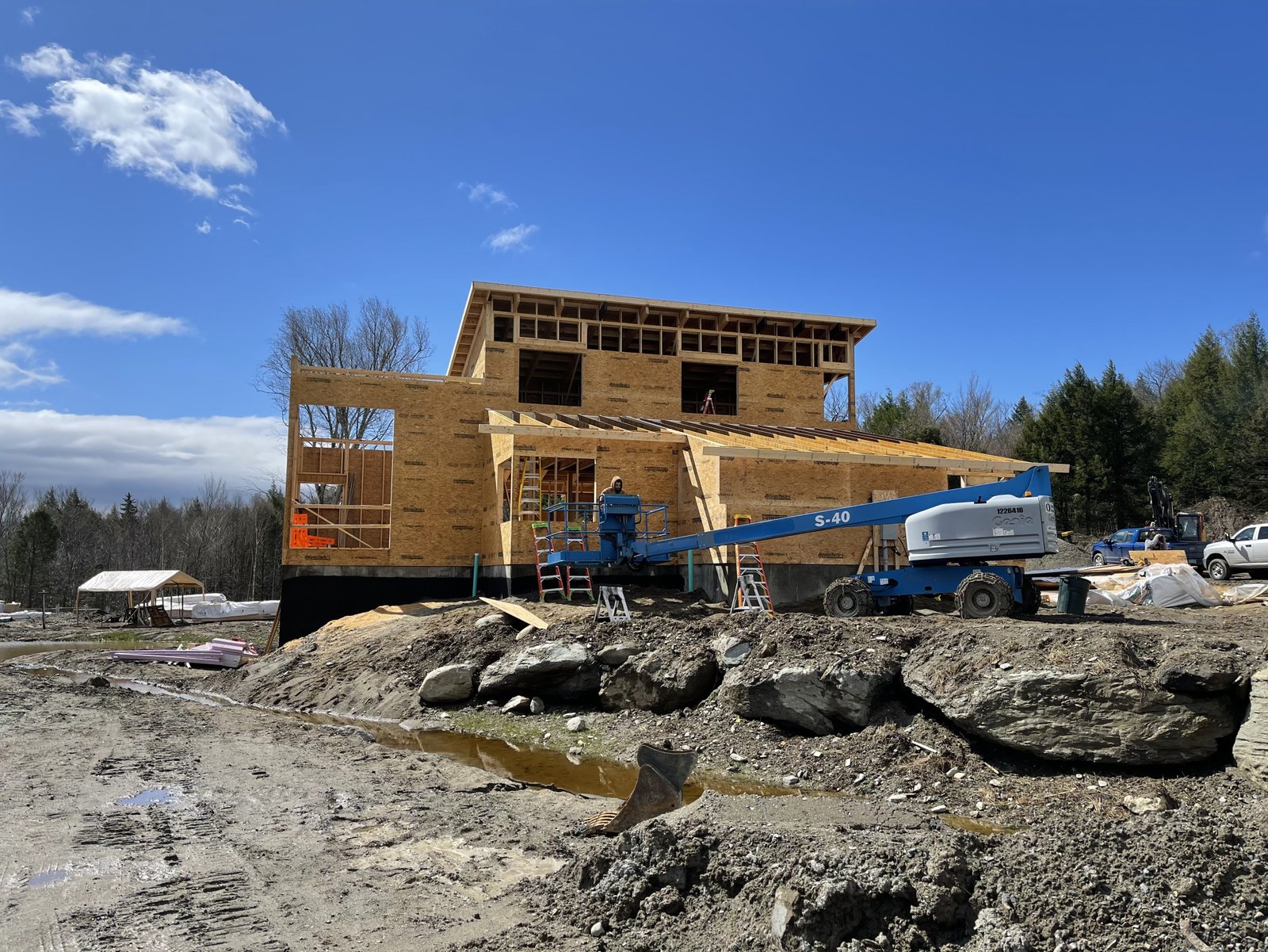 Two-story wood-framed home under construction by Lakeshore Construction on a Vermont hillside, with a boom lift on site